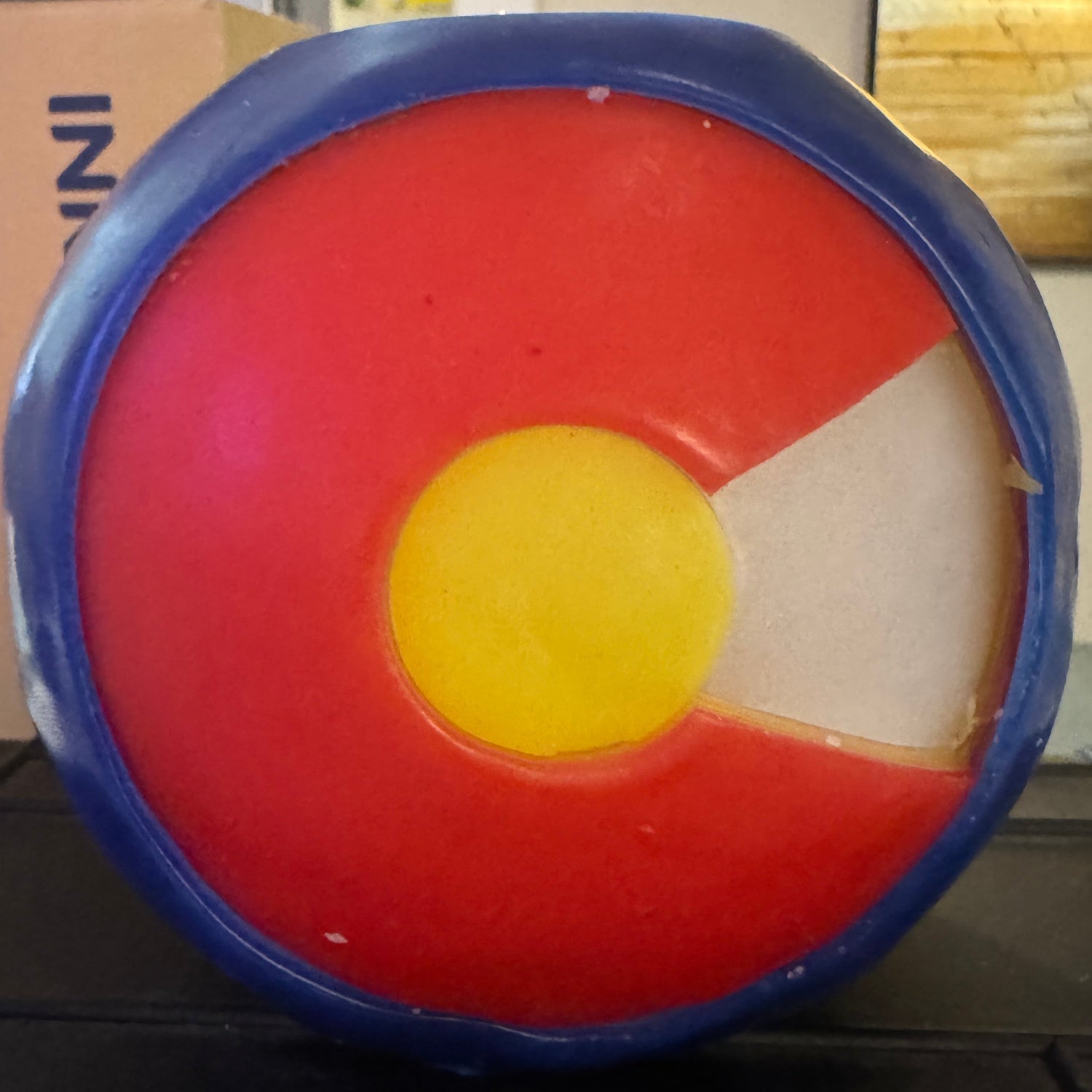 Hand carved 4" Sphere candle with the Colorado Flag using red, yellow, white, and blue wax featured. It is shown lit externally.