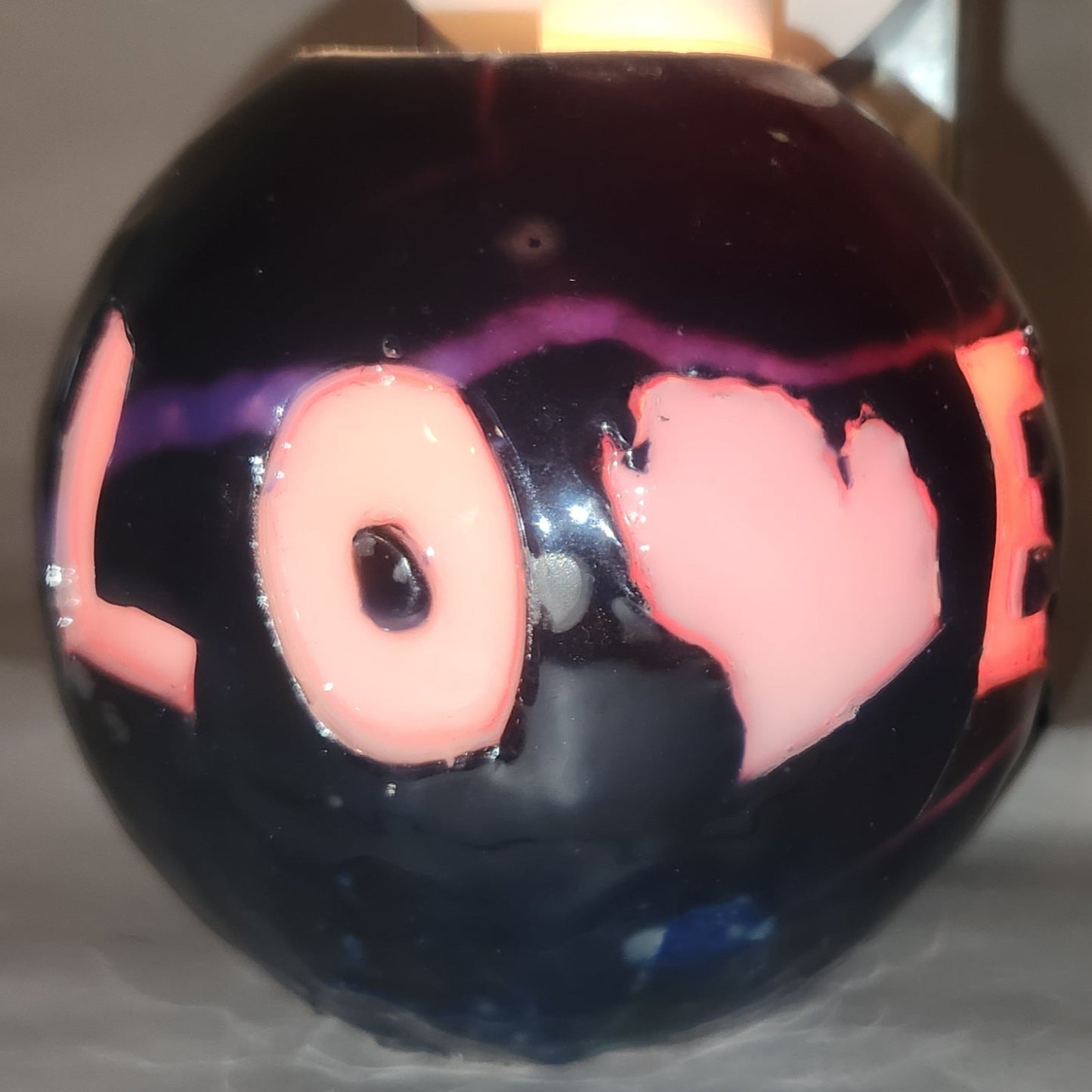 Hand carved spherical candle with black outside and "LOVE" carved in the sign with the "V" being replaced by the outline of state of Michigan featured. It is shown glowing from within.