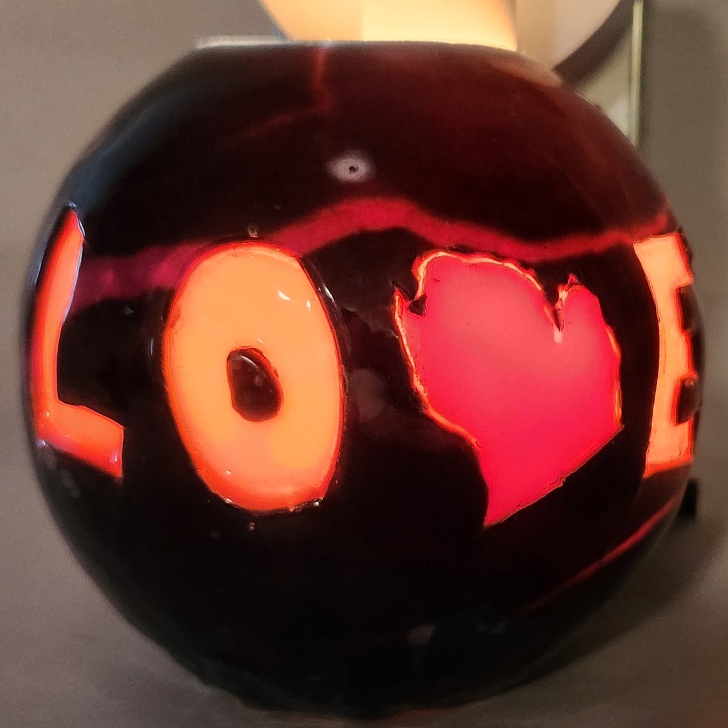 Hand carved spherical candle with black outside and "LOVE" carved in the sign with the "V" being replaced by the outline of state of Michigan featured. It is shown glowing from within.