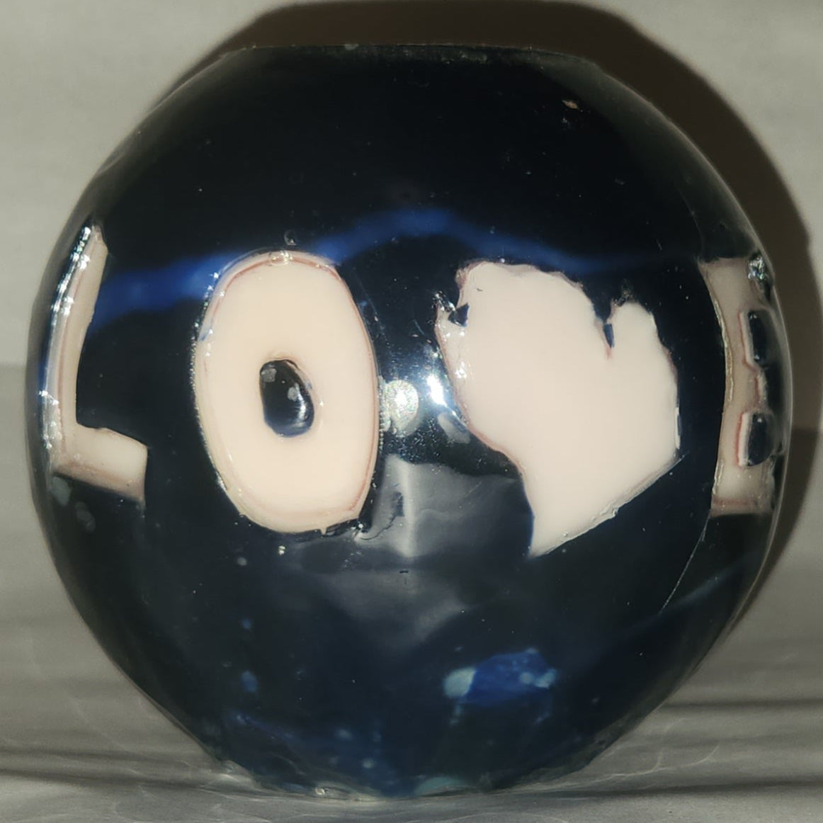 Hand carved spherical candle with black outside and "LOVE" carved in the sign with the "V" being replaced by the outline of state of Michigan featured. It is shown being lit externally.