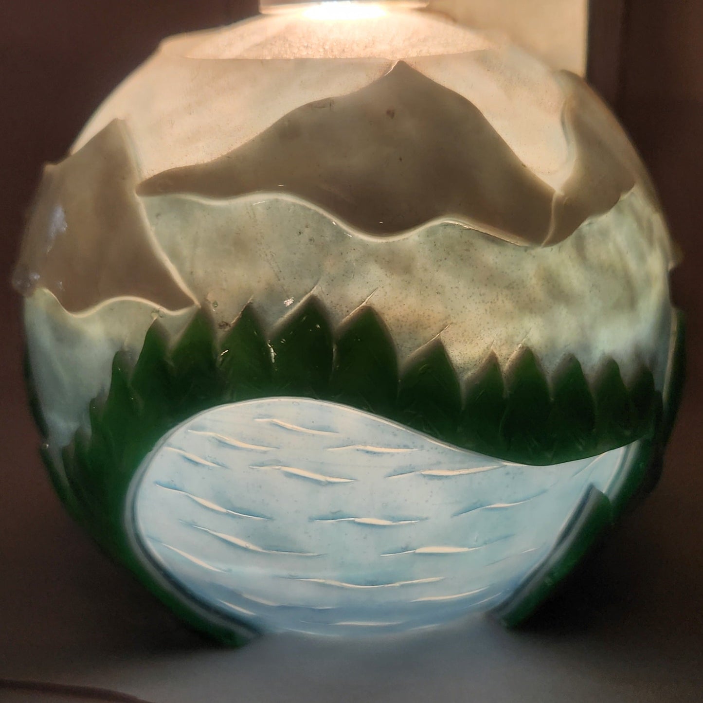 Hand carved spherical candle with rippling lake, trees, mountains and sky featured. It is lit from the top by a white light and the candle glows from within.