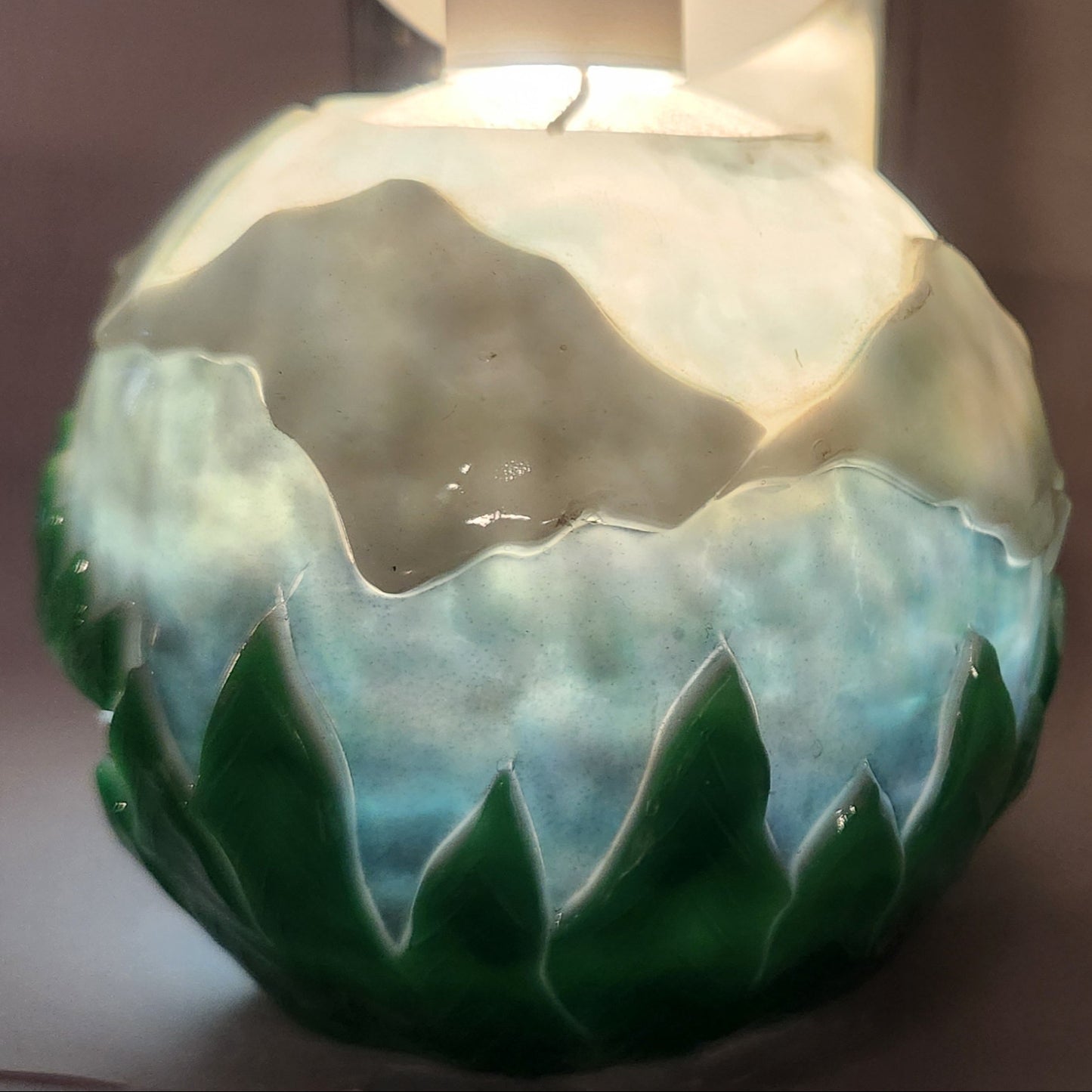Hand carved spherical candle with trees, mountains and sky featured. It is lit from the top by a white light and the candle glows from within.