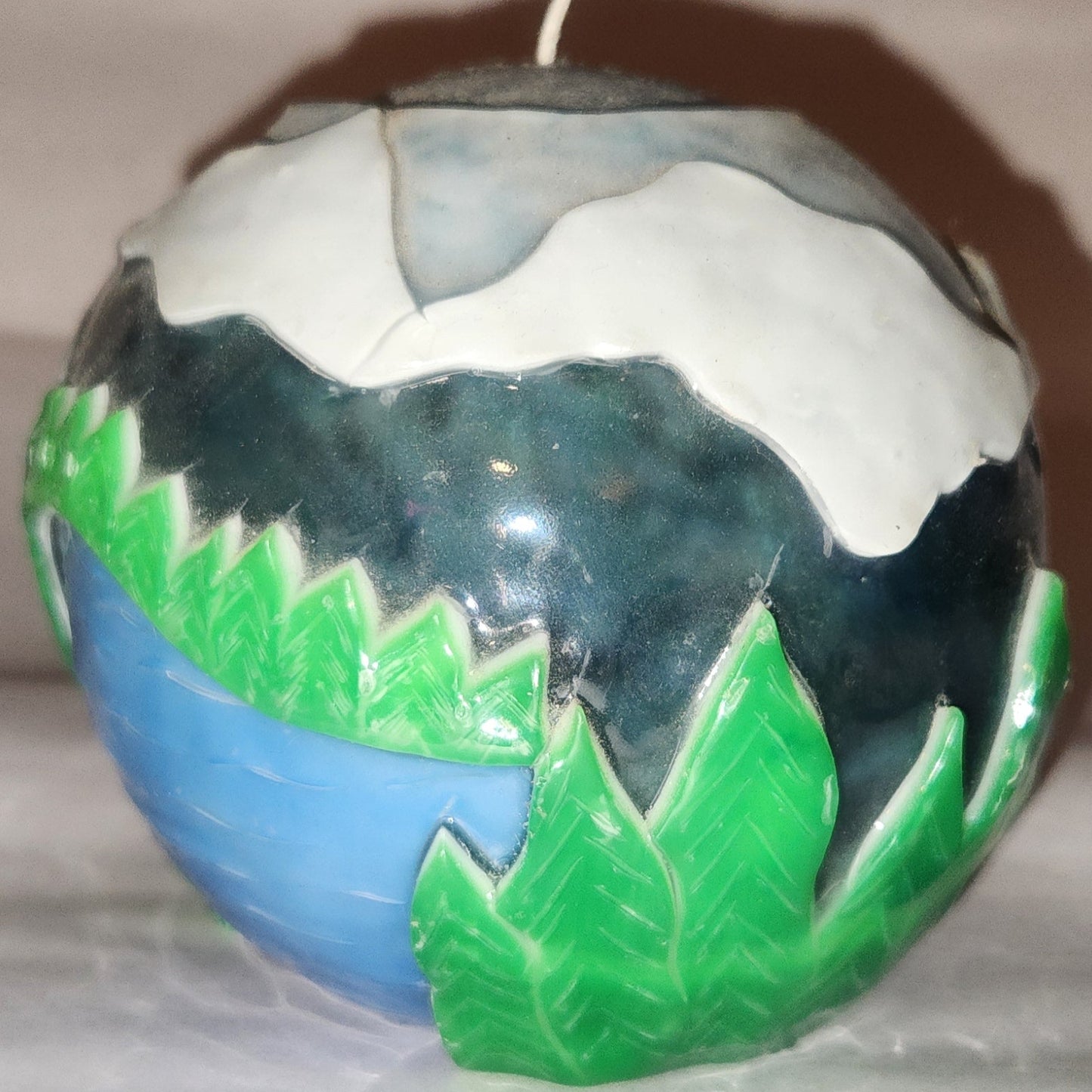 Hand carved spherical candle with trees, mountains and sky featured.