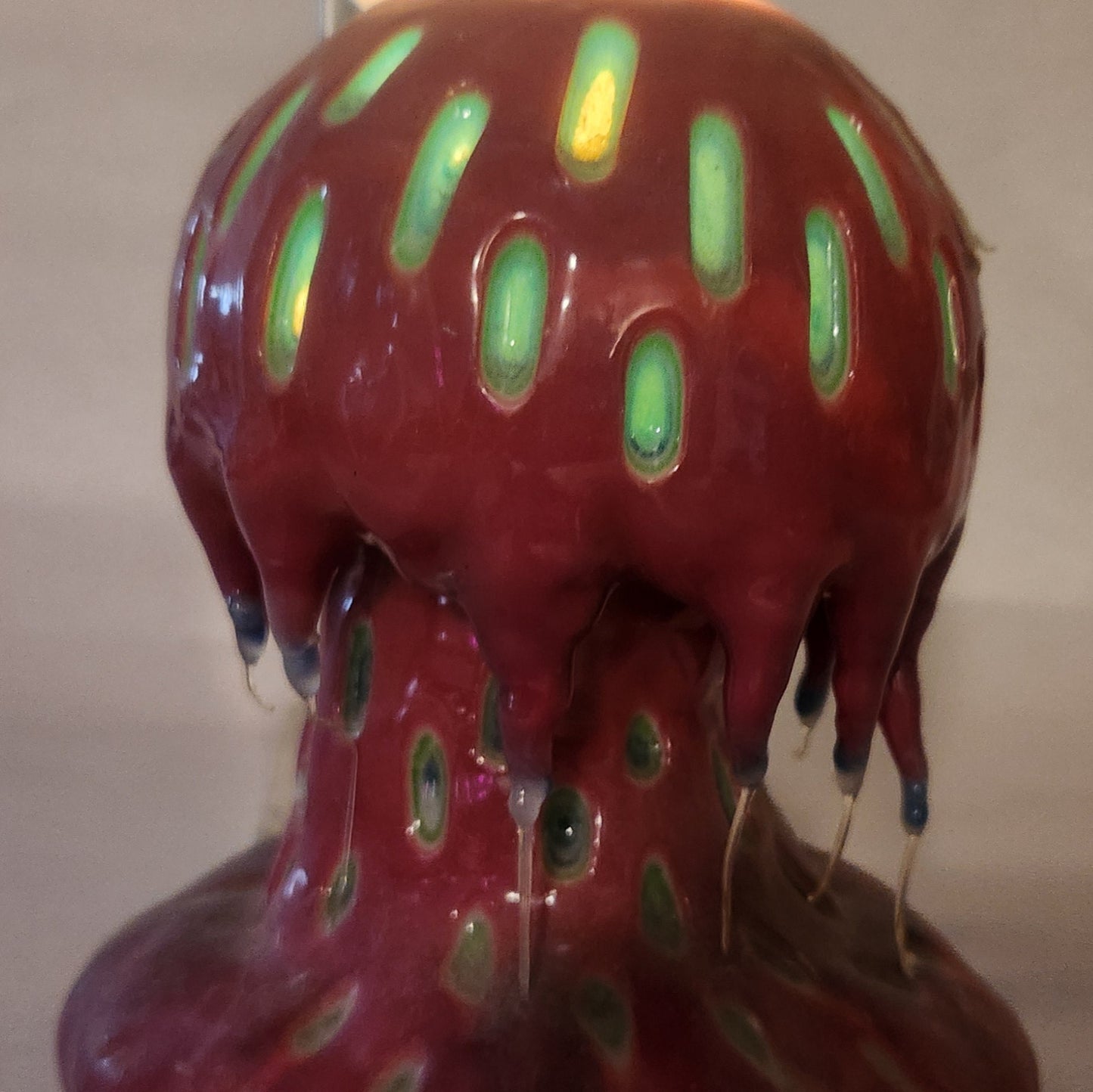 Hand carved Mushroom shaped candle with red outside and layered spots carved from the cap and stem with wax drips coming off the cap featured. It is shown glowing from within.