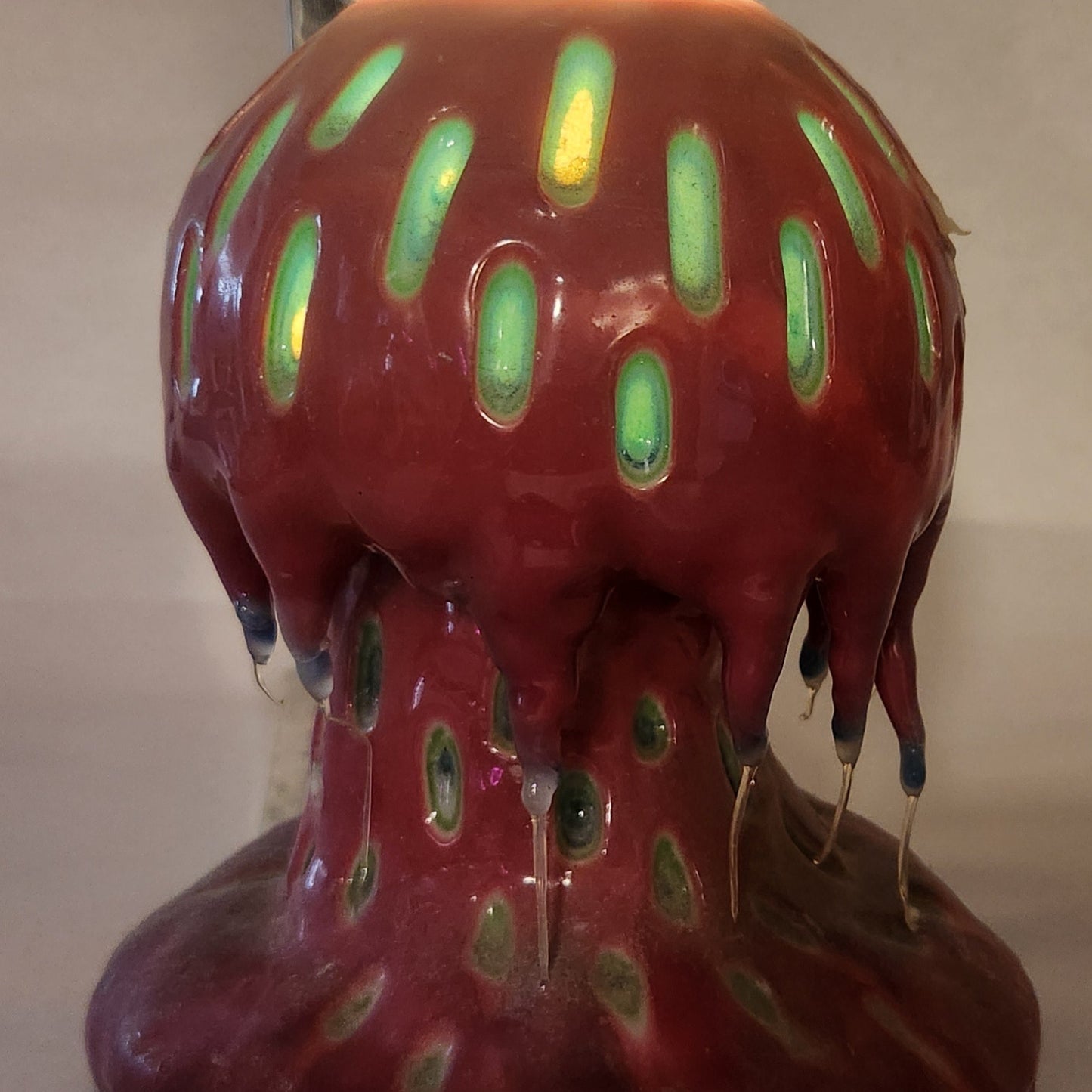 Hand carved Mushroom shaped candle with red outside and layered spots carved from the cap and stem with wax drips coming off the cap featured. It is shown glowing from within.