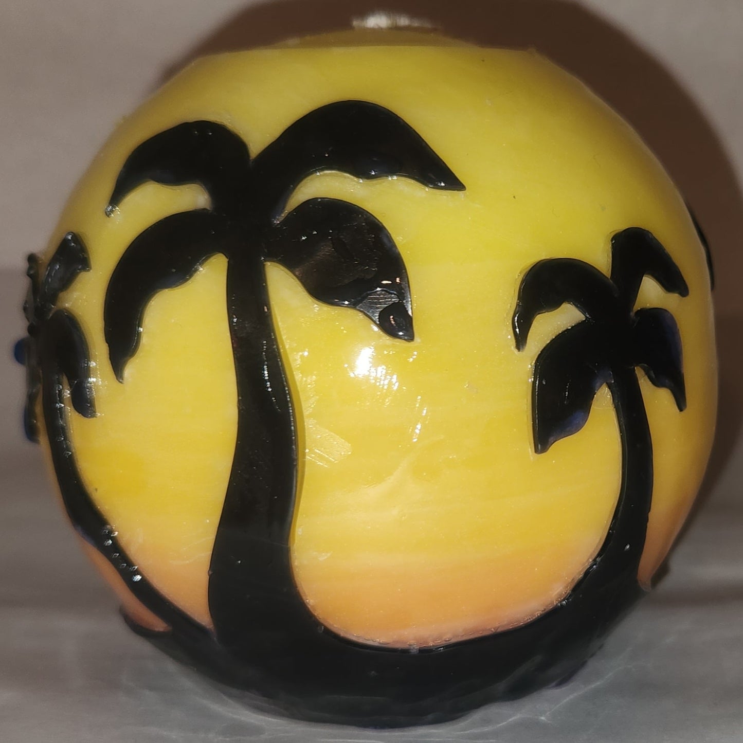 Hand carved spherical candle with Orange sunset and silhouetted palm trees featured. Shown lit externally.
