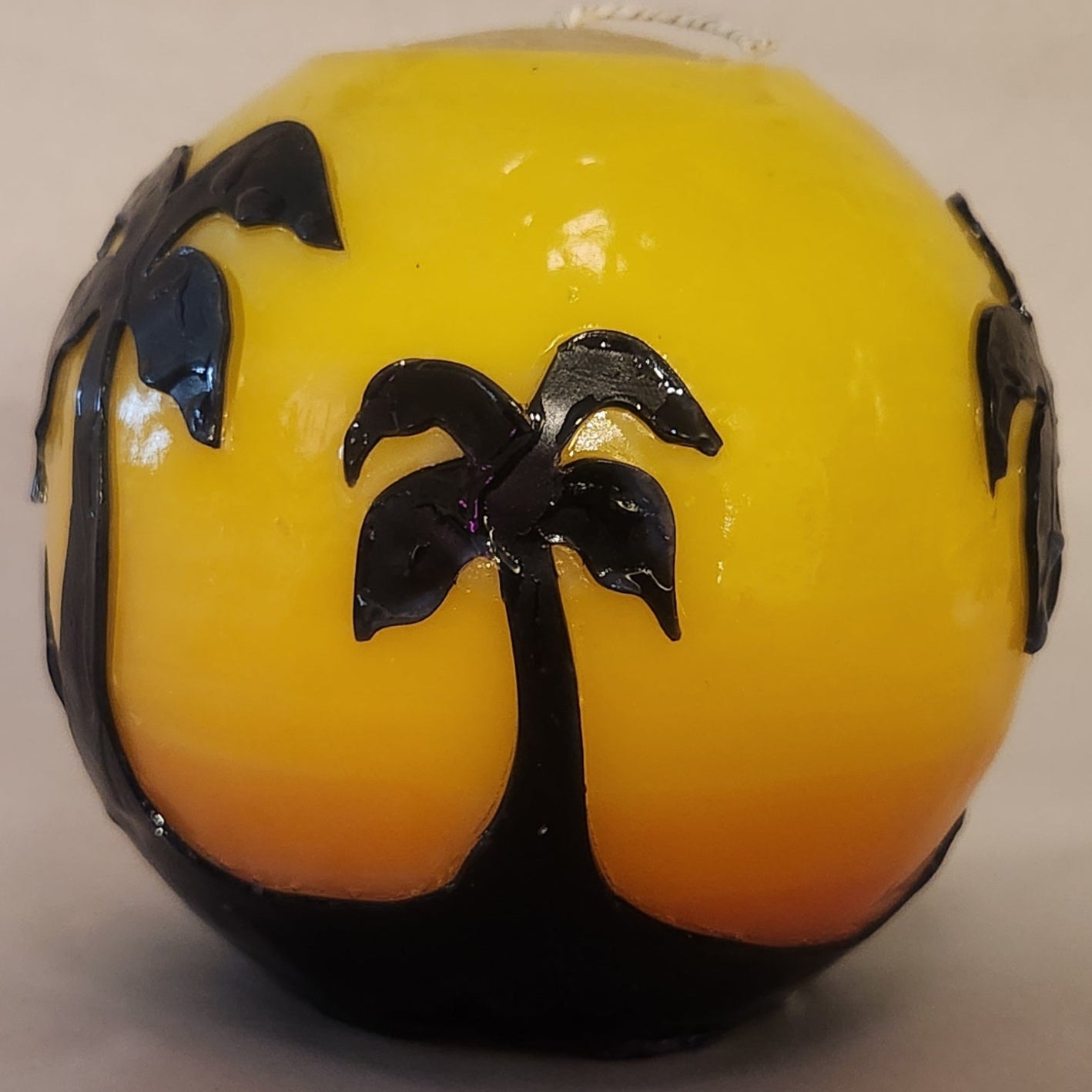 Hand carved spherical candle with Orange sunset and silhouetted palm trees featured. Shown lit externally.