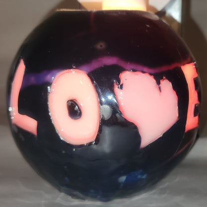 Hand carved spherical candle with black outside and "LOVE" carved in the sign with the "V" being replaced by the outline of state of Michigan featured. It is shown glowing from within.