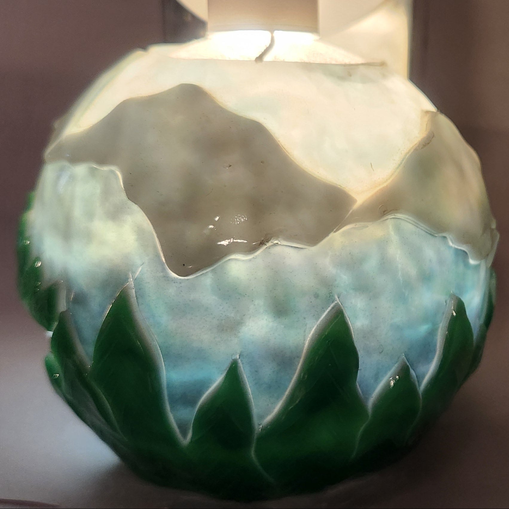 Hand carved spherical candle with trees, mountains and sky featured. It is lit from the top by a white light and the candle glows from within.