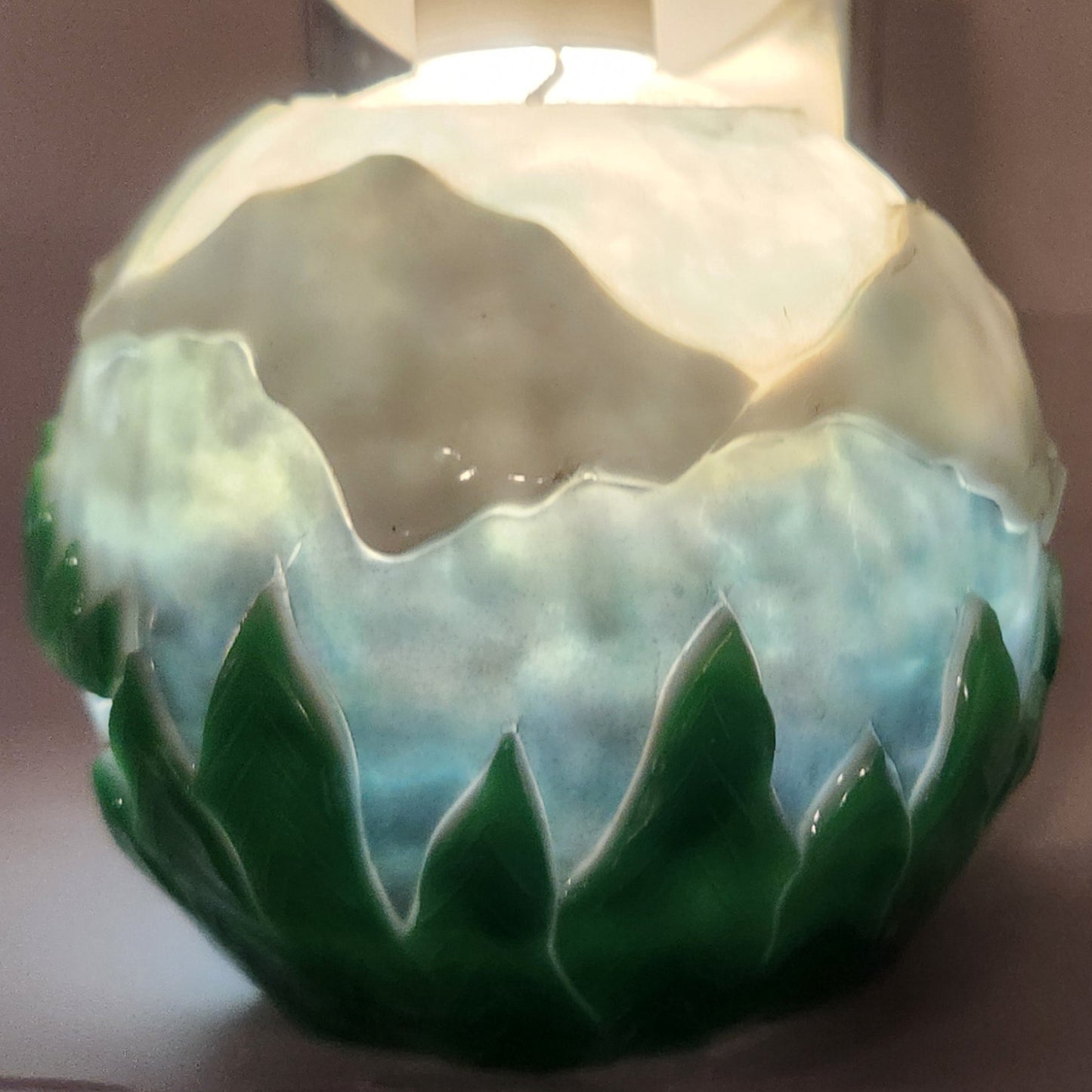 Hand carved spherical candle featuring trees, mountains and sky featured. It is lit from the top by a white light and the candle glows from within.