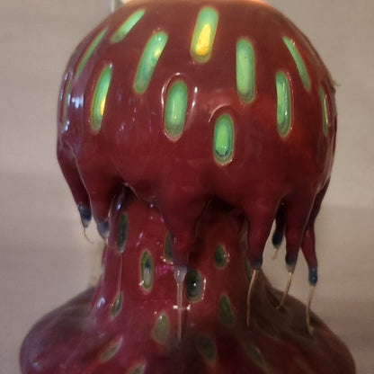 Hand carved Mushroom shaped candle with red outside and layered spots carved from the cap and stem with wax drips coming off the cap featured. It is shown glowing from within.