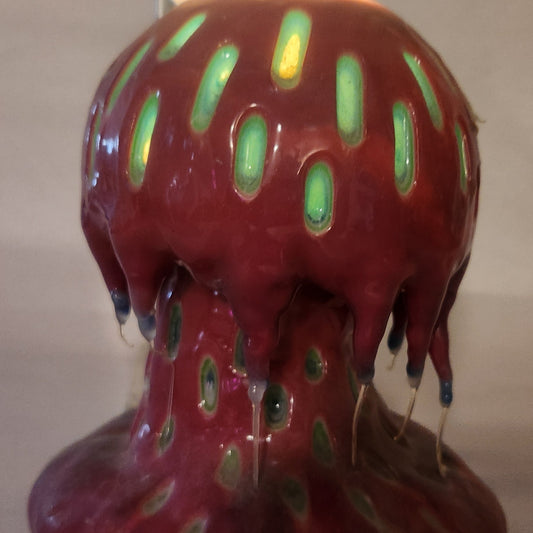 Hand carved Mushroom shaped candle with red outside and layered spots carved from the cap and stem with wax drips coming off the cap featured. It is shown glowing from within.