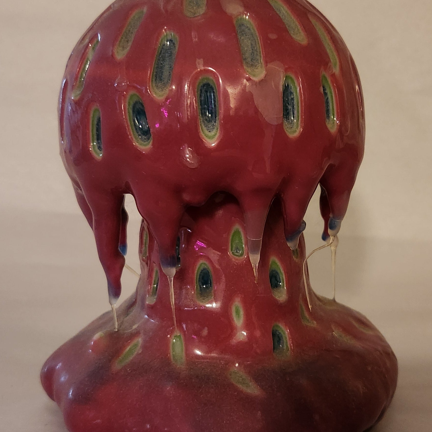 Hand carved Mushroom shaped candle with red outside and layered spots carved from the cap and stem with wax drips coming off the cap featured. It is shown lit externally.